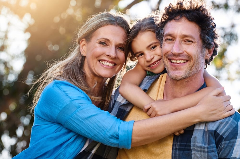 Portrait of a joyful family of three smiling and embracing each other outdoors in warm sunlight – Advanced Torrance Dental Group